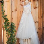A detailed wedding dress hanging on a wooden fence at Fleetwood Farm Winery.