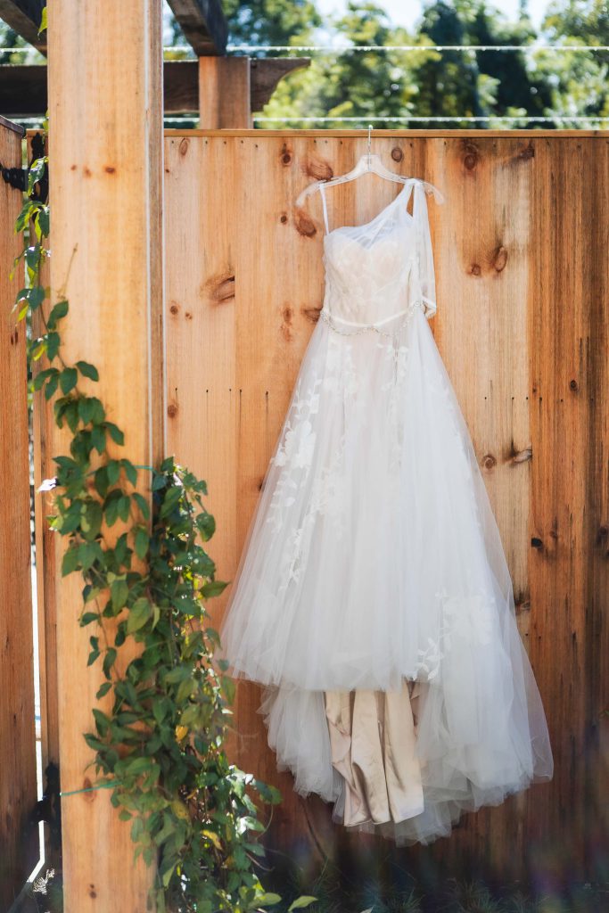 A detailed wedding dress hanging on a wooden fence at Fleetwood Farm Winery.