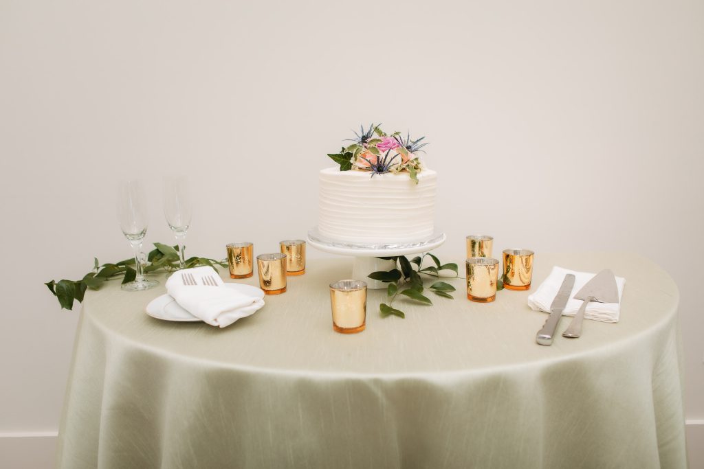 A wedding cake on a table with candles, flowers, and exquisite detail.