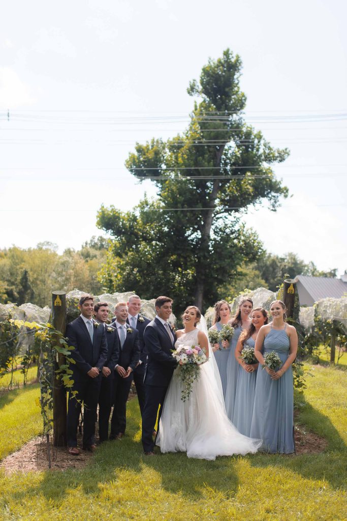 The wedding party, dressed in their finest attire, poses for a portrait amidst the scenic beauty of Fleetwood Farm Winery.