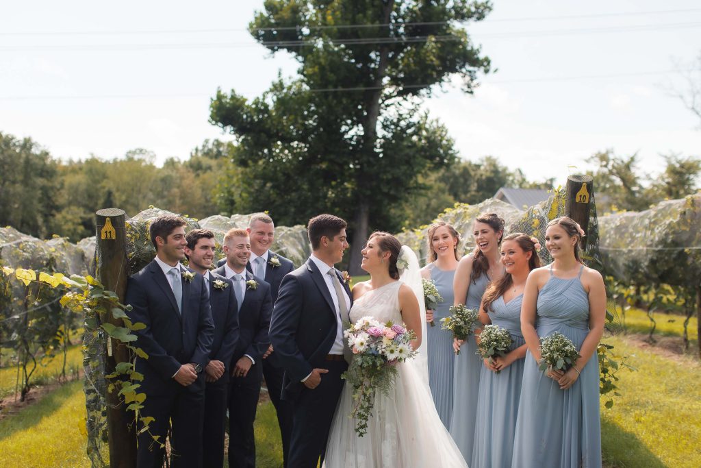 A portrait of bridesmaids and groomsmen standing in a vineyard at Fleetwood Farm Winery.