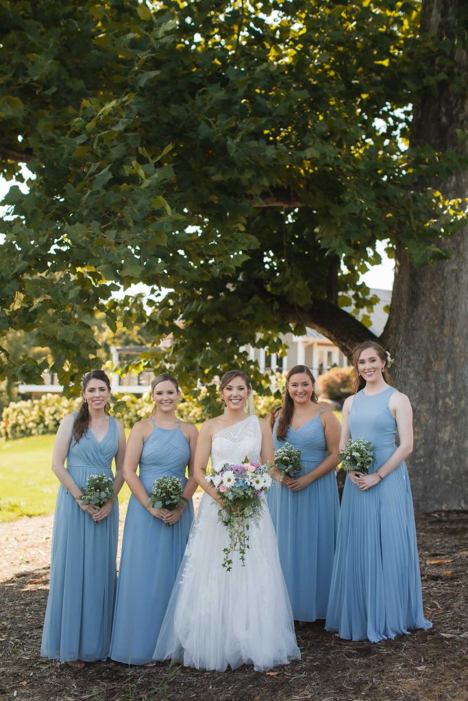 A wedding portrait at Fleetwood Farm Winery, with the bride and her bridesmaids posing in front of a tree.