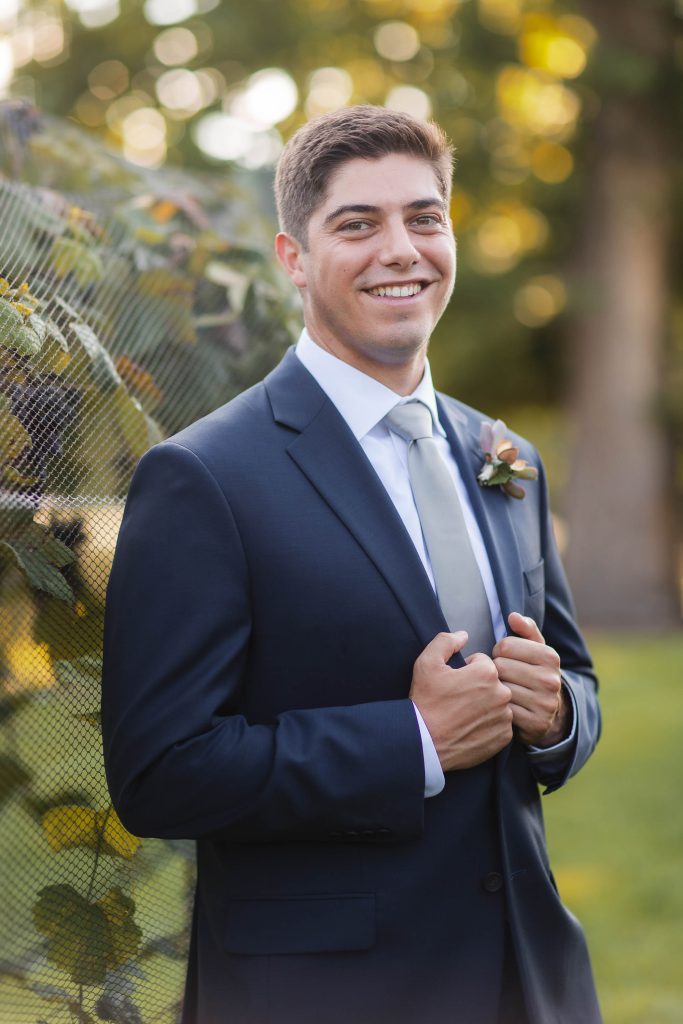 A man in a suit is smiling in front of a fence at Fleetwood Farm Winery.