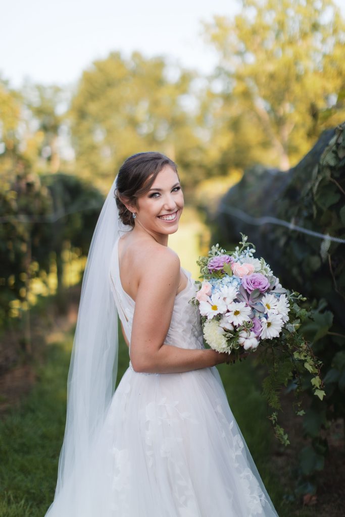 A bride holding a wedding bouquet in a vineyard at Fleetwood Farm Winery.