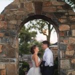 A bride and groom share a tender moment in front of a stone archway at Fleetwood Farm Winery during their portrait session on their wedding day.