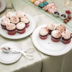 A plate of cupcakes on a table at a wedding reception, next to a glass of wine from Fleetwood Farm Winery.