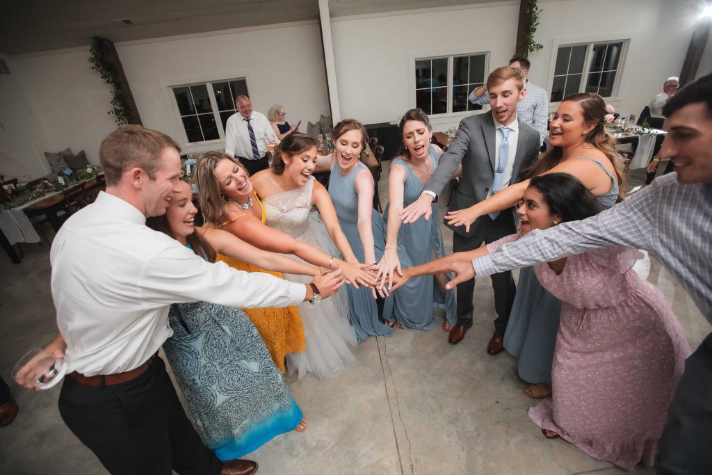 A group of bridesmaids and groomsmen holding hands in a wedding circle at Fleetwood Farm Winery.