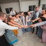 A group of bridesmaids and groomsmen holding hands in a wedding circle at Fleetwood Farm Winery.