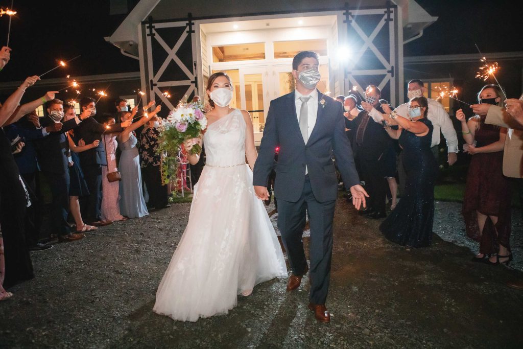 A bride and groom walk out of Fleetwood Farm Winery with sparklers, ready to celebrate their wedding reception.