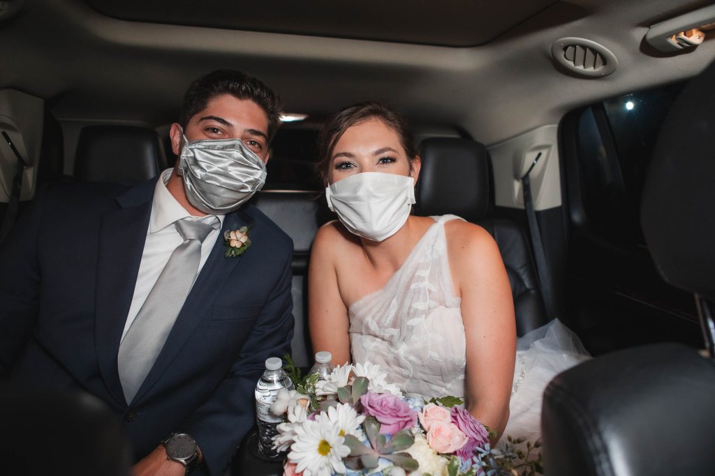 A bride and groom wearing face masks on their wedding day in a car driving towards the reception at Fleetwood Farm Winery.