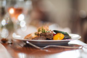 A plate of food on a table next to a glass of wine provided by Main Event Catering.