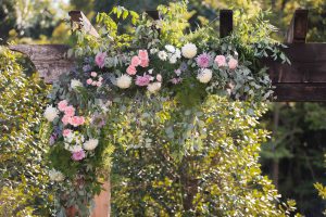 A wedding arch decorated with flowers and greenery by event vendor, The Pink Poppy.