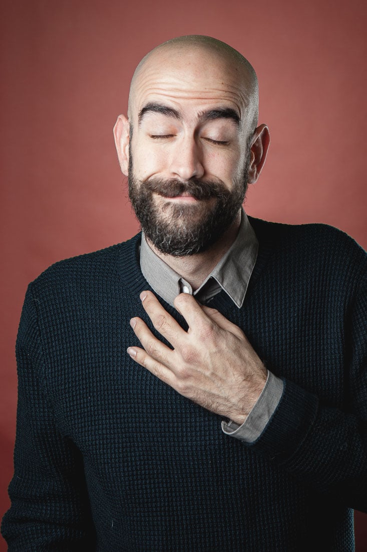 A bald man with his hand on his chest.