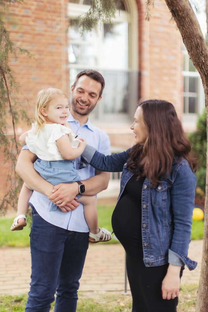 A pregnant woman posing for a family portrait in front of a brick building.