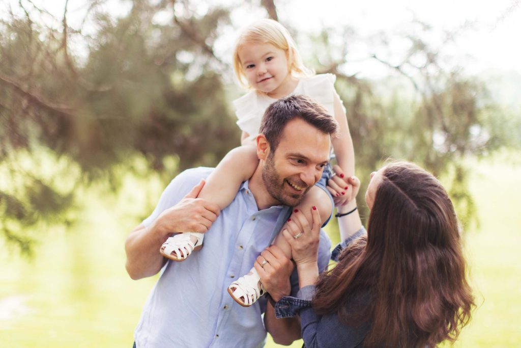 A family is holding their baby in their arms in a park.