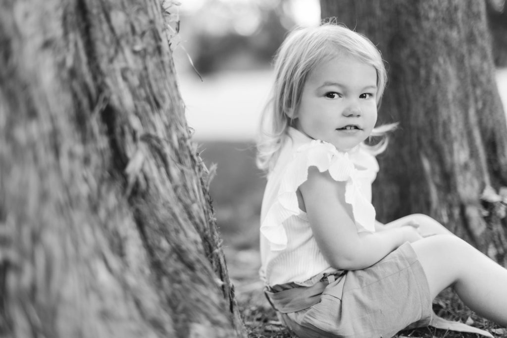 A black and white family portrait of a little girl sitting under a tree.