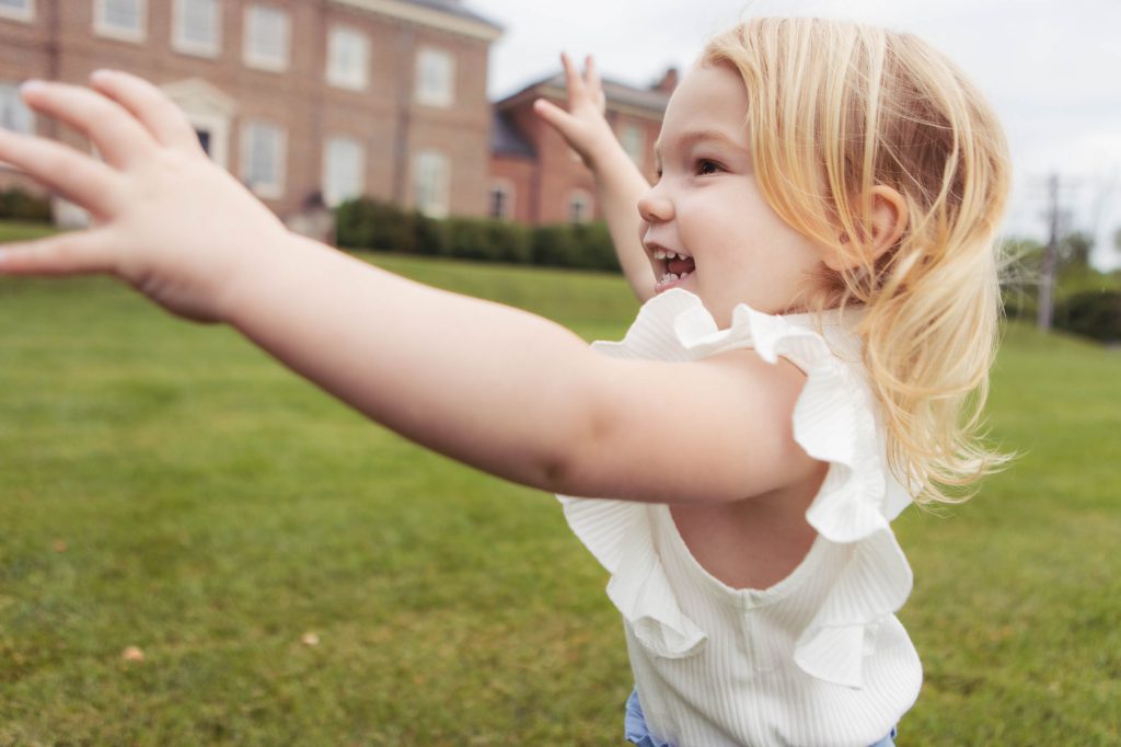 A little girl is throwing her arms up in the air during a family portrait session at a Bel Air mansion.