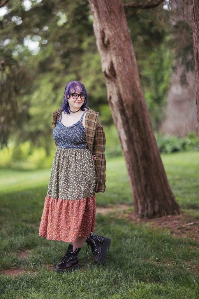 A High School Senior in a plaid dress standing next to a tree for her graduation portrait.