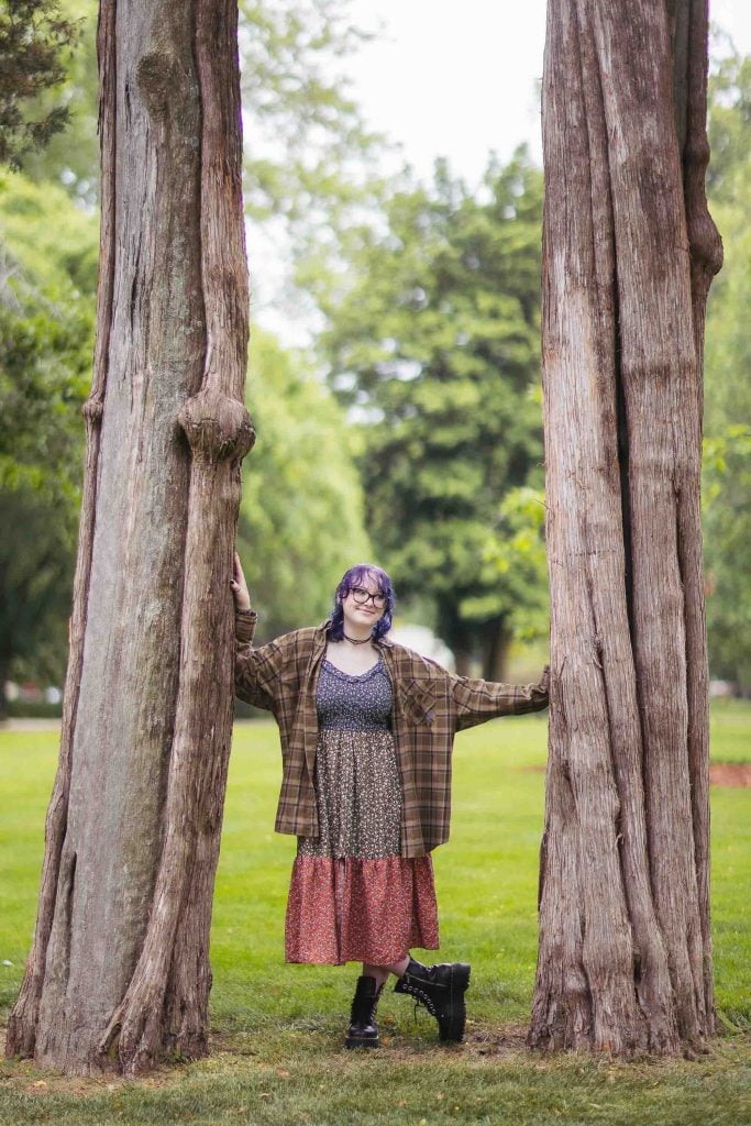 A High School Senior is leaning against two trees in front of a Bel Air Mansion.
