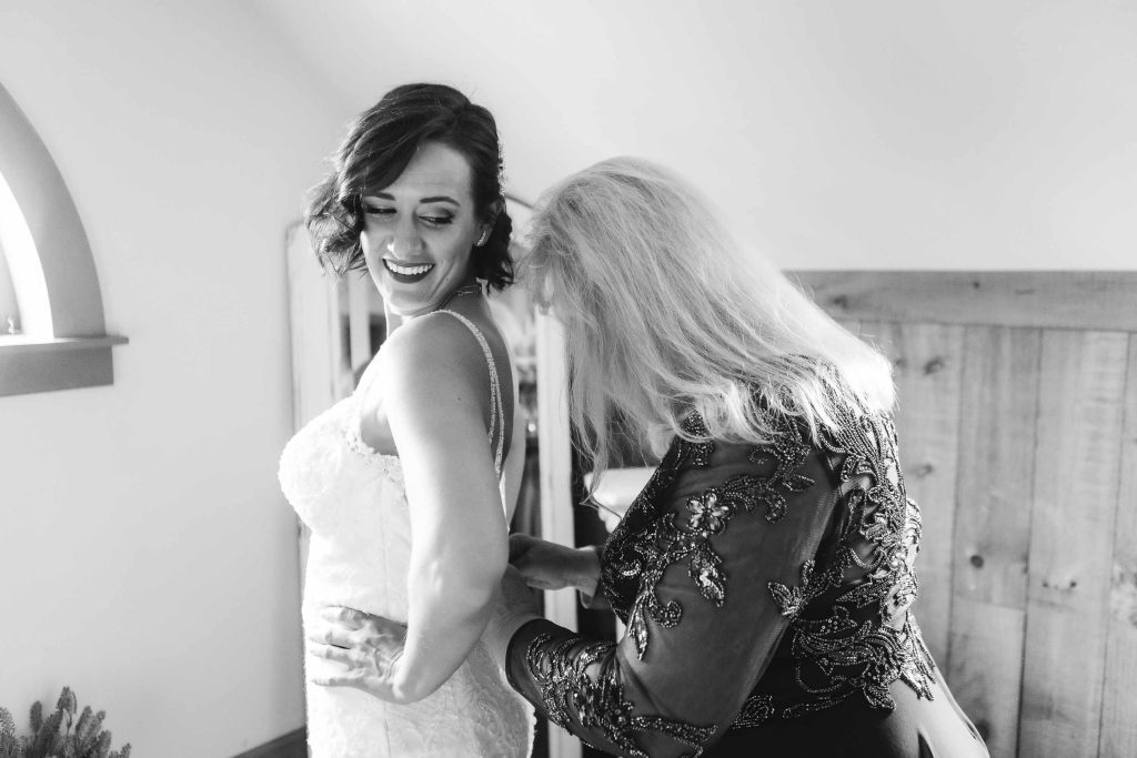 A candid photo capturing the wedding preparation of a bride helping her mother put on her wedding dress.