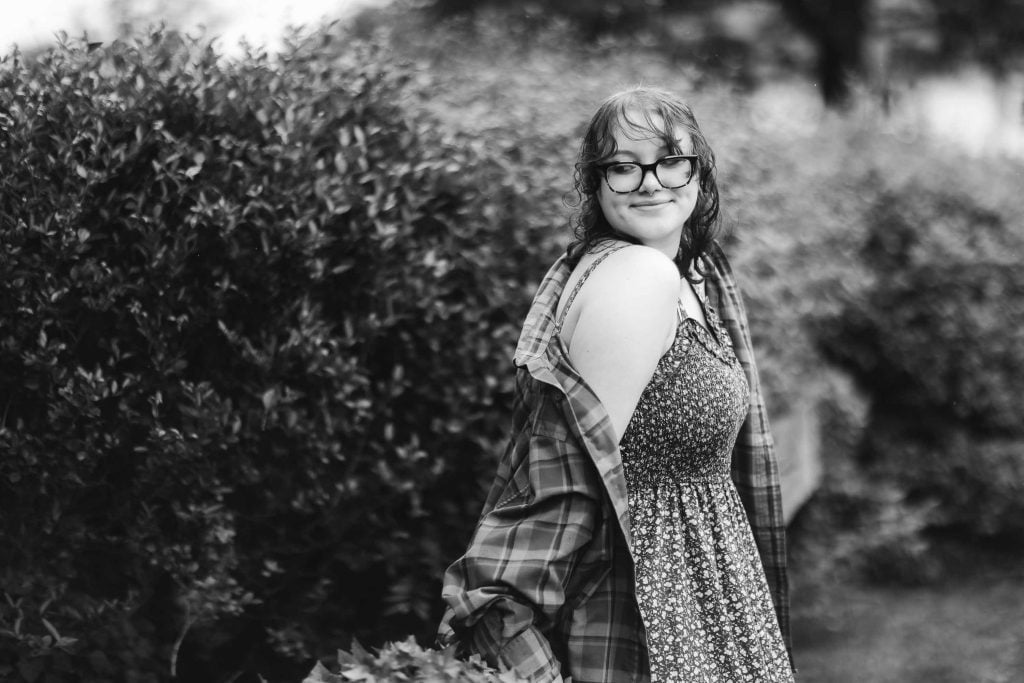 A black and white portrait of a high school senior wearing glasses and a dress.