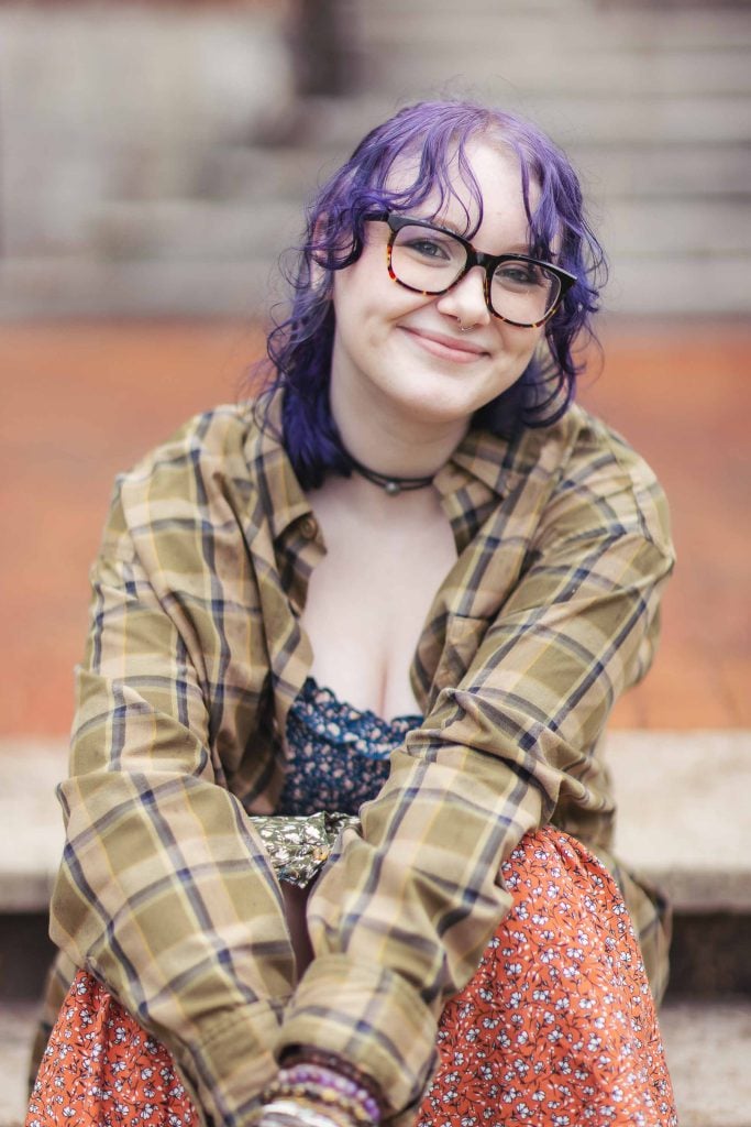 A High School Senior with purple hair and glasses sitting on steps.