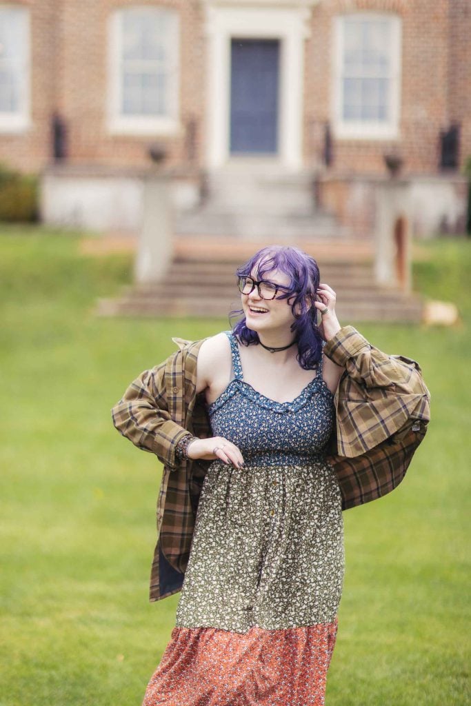 A high school senior in a plaid dress standing in front of a house.