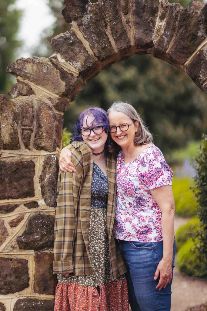 Two high school senior women posing in front of a stone arch for their graduation.