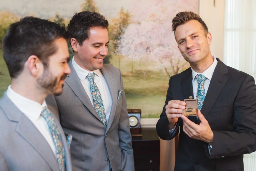 Three groomsmen preparing for a wedding, looking at a candidly captured wedding ring.