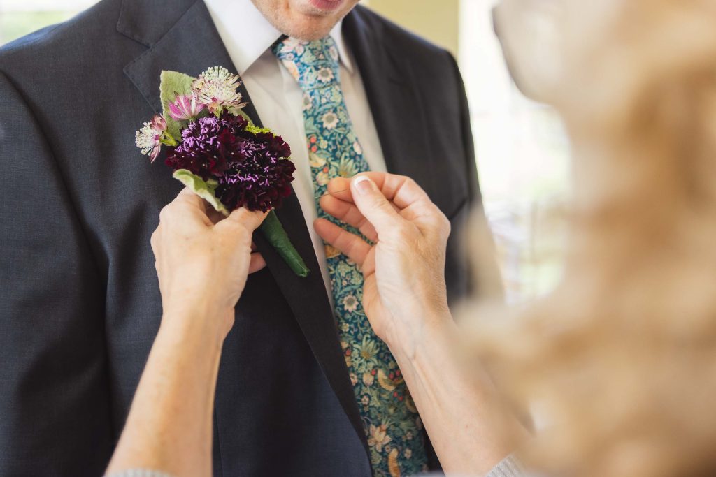 Candid wedding preparation with a man putting on a boutonniere.