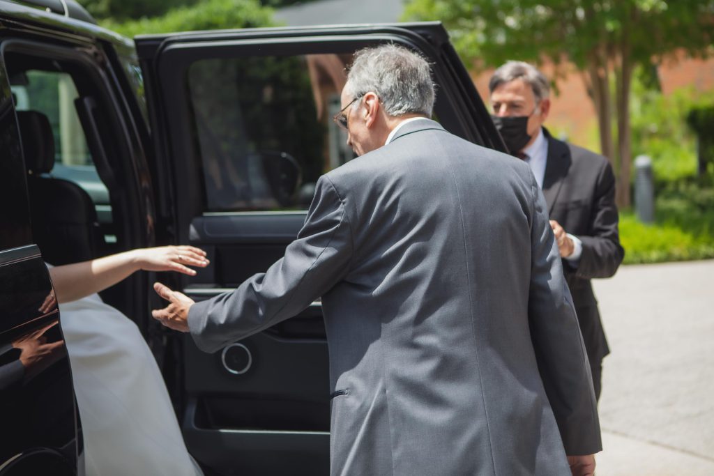 A candid wedding preparation moment: A bride and groom emerging from a black limo.