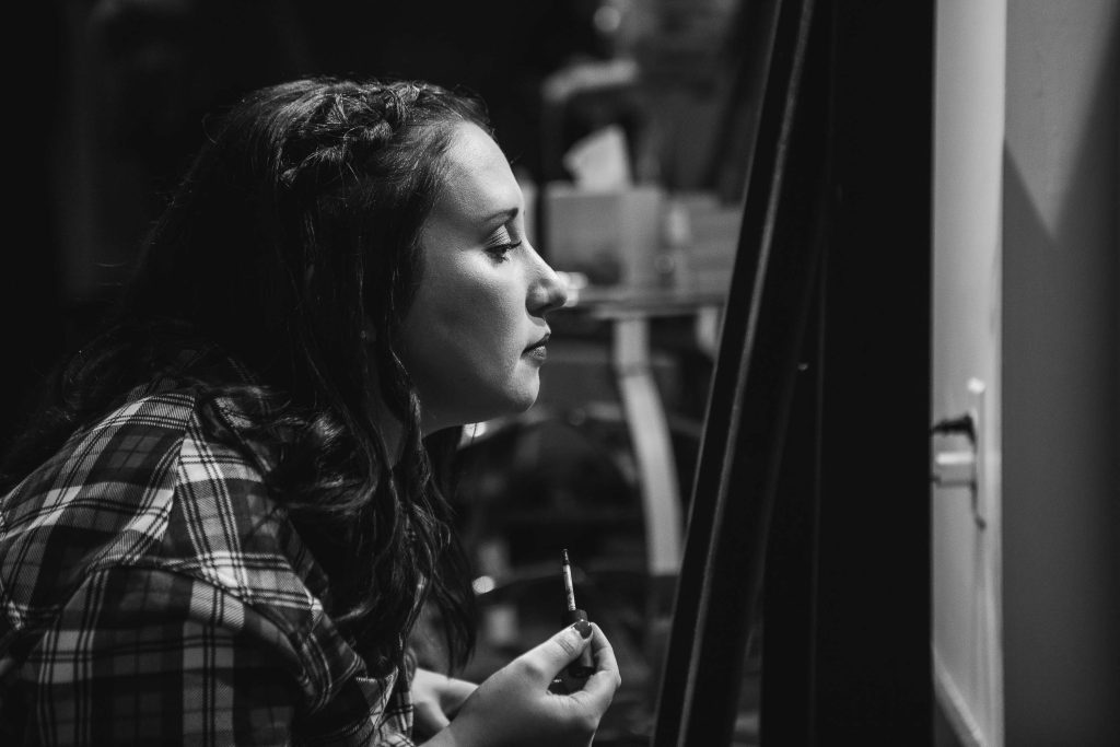 A candid black and white photo of a woman preparing for a wedding while looking at a mirror.