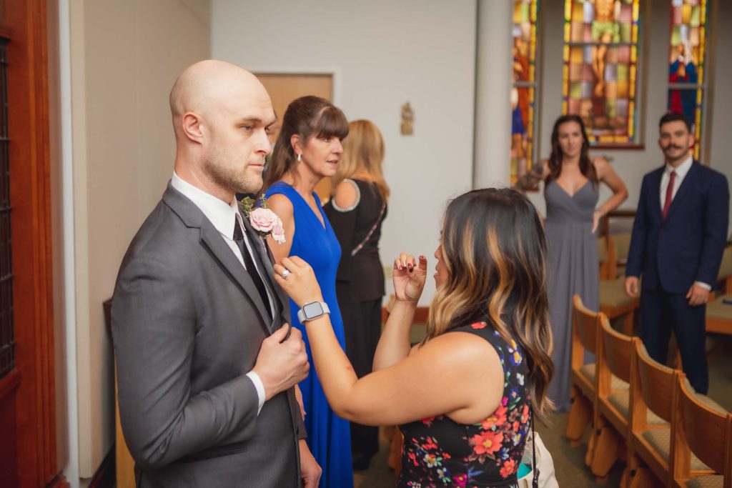 A man is candidly preparing a boutonniere for a wedding ceremony in a church.