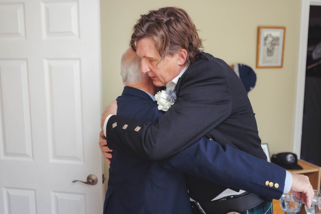 A man in a kilt is hugging another man before a wedding.
