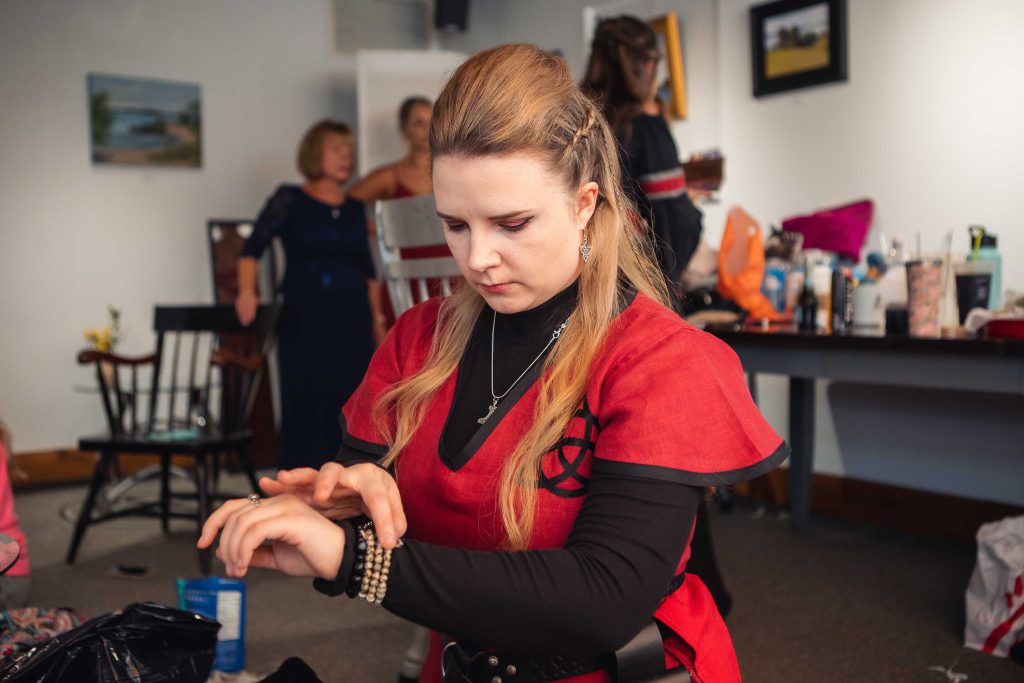 A woman in a red dress is candidly adjusting her purse during wedding preparation.