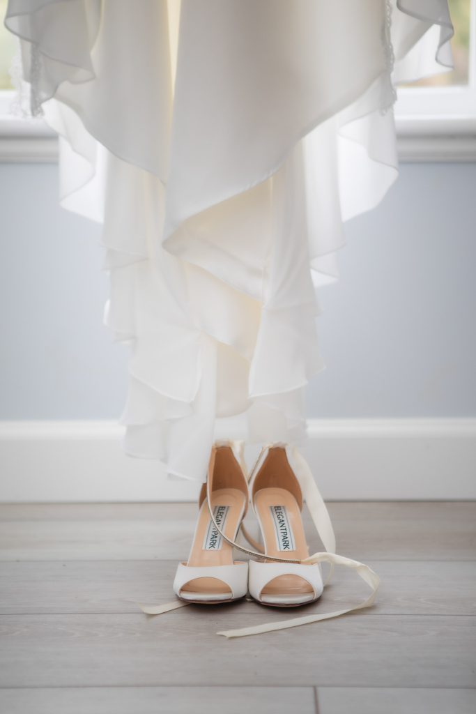 A bride's wedding dress and shoes captured in intricate detail against a window backdrop.