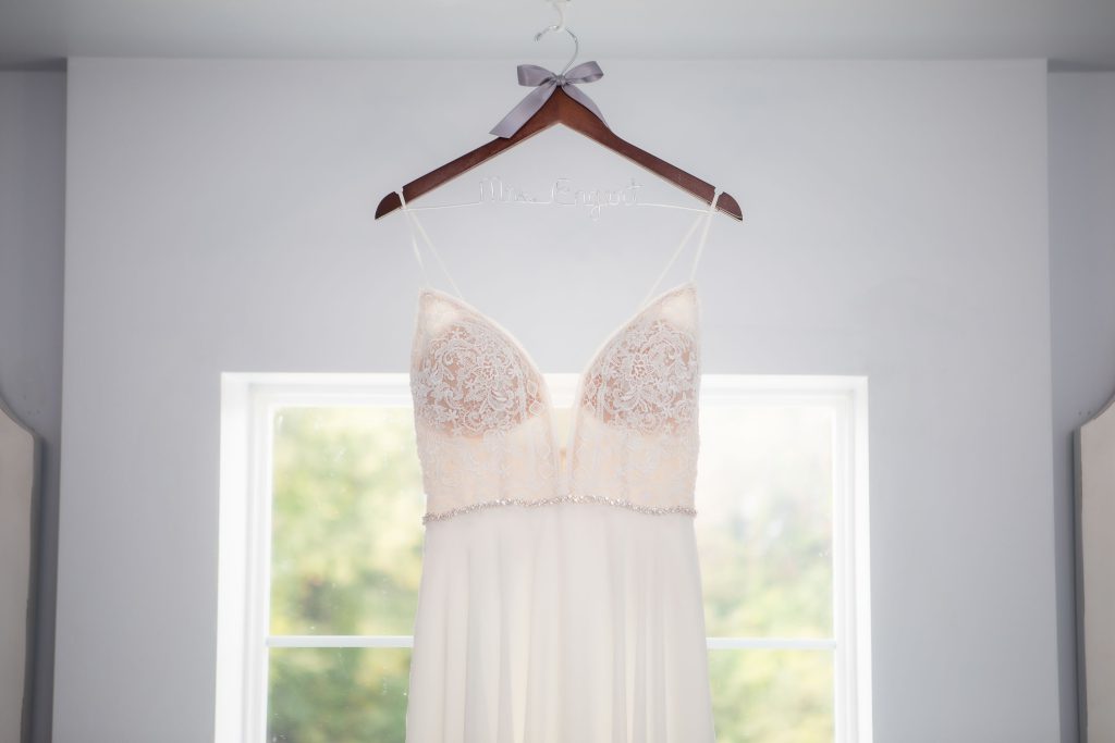 A detailed wedding dress hanging in front of a window.