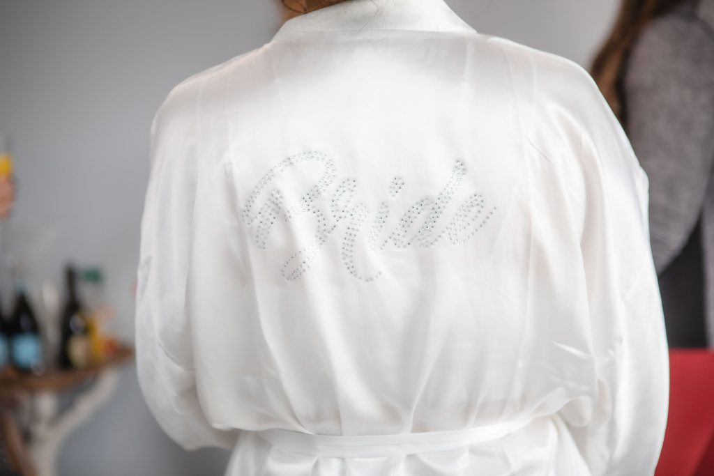 A bride in a white robe showcasing wedding details.