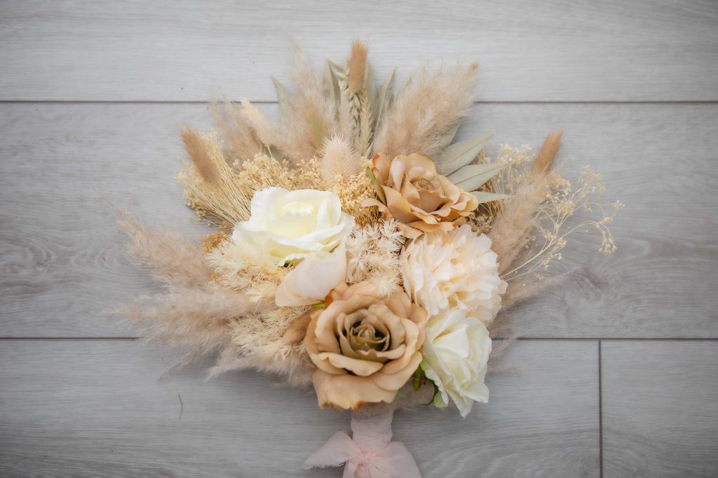 A detailed bouquet of dried grass and roses adorning a wooden floor at a wedding.