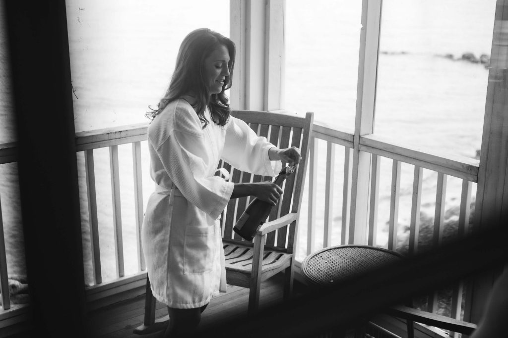 A woman in a robe preparing for her wedding, sitting on a chair near the ocean.