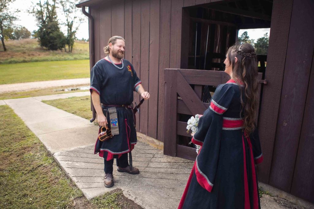A man and woman dressed in viking costumes are standing in front of a barn, preparing for their wedding.