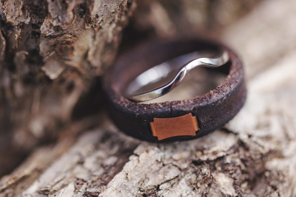 A leather wedding ring is sitting on top of a piece of wood, showcasing intricate details.