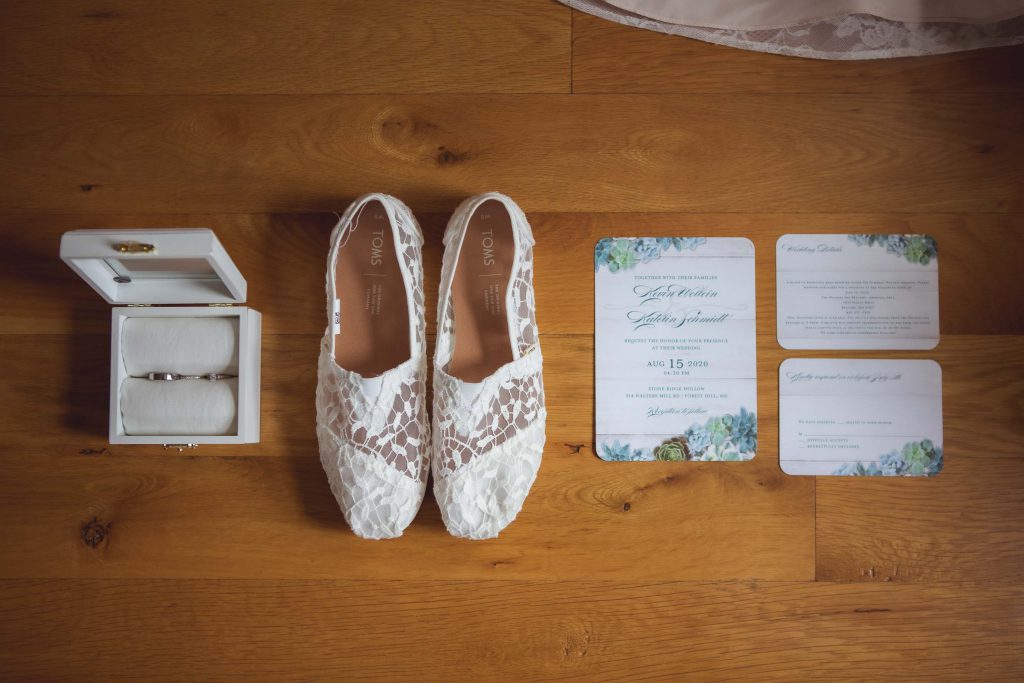Wedding details featuring a pair of wedding shoes and a wedding ring on a wooden floor.