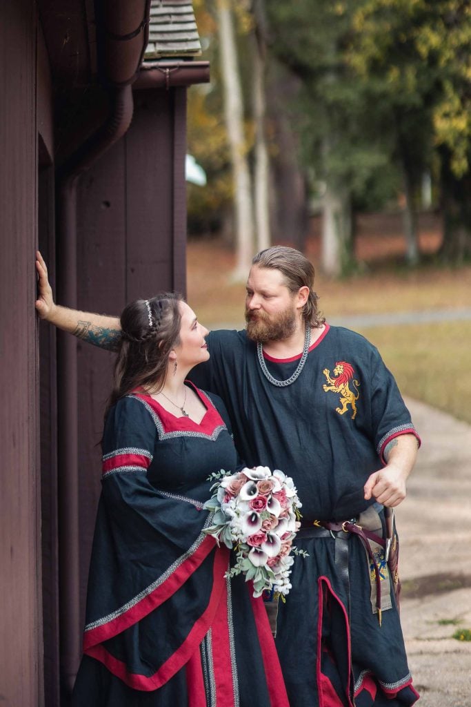 A couple dressed in medieval wedding attire pose for a portrait.