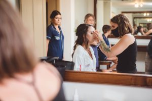 A candid bride preparing for her wedding, getting her makeup done in front of a mirror.
