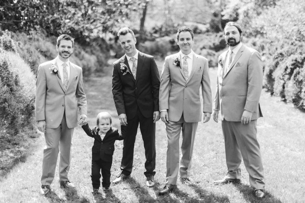 Black and white wedding portrait of groomsmen posing with a little boy.