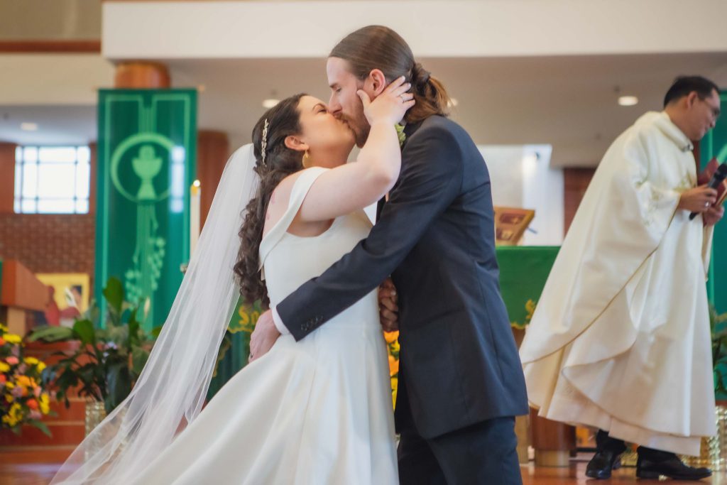 A wedding ceremony featuring a bride and groom sharing a kiss in front of a priest.