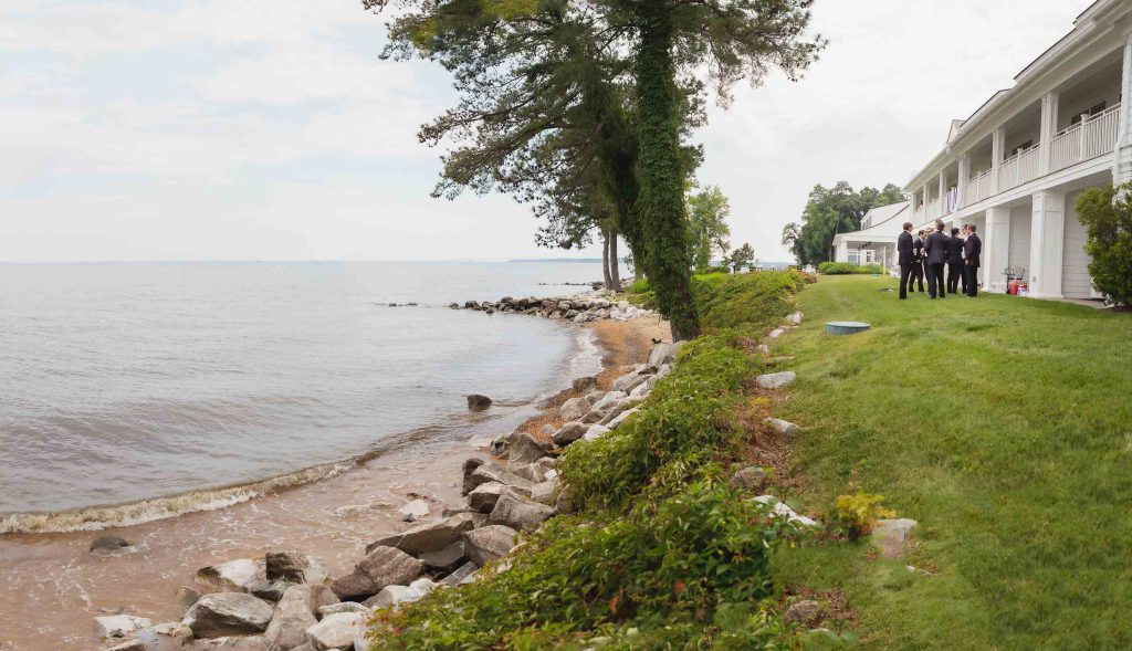 A group of people candidly preparing for a wedding near a building on the shore.