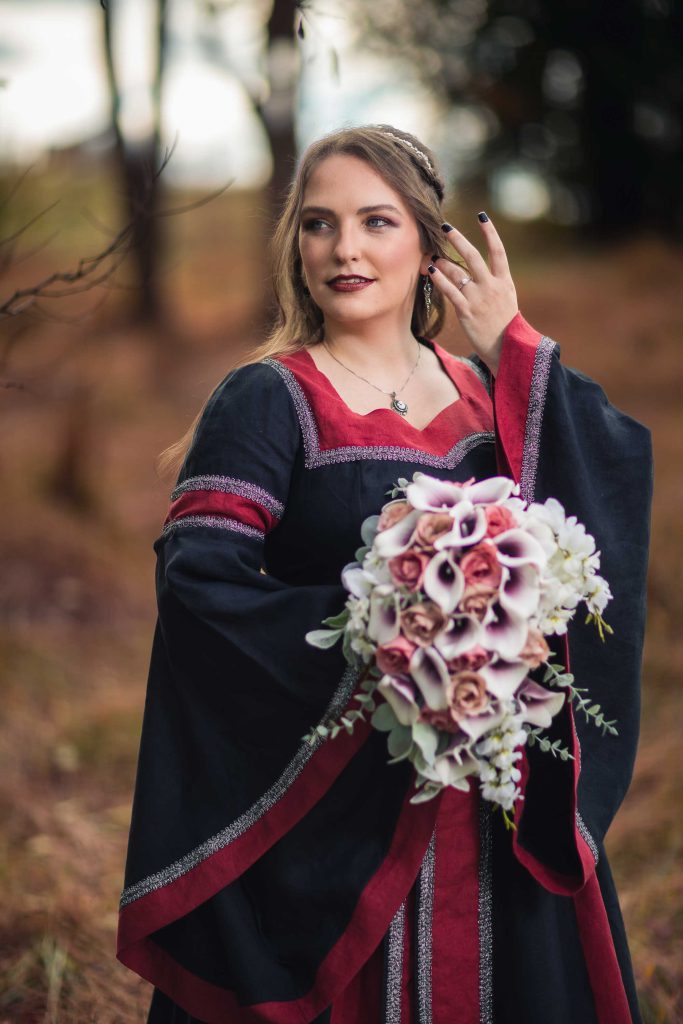 A bride in a red and black wedding dress holding a bouquet for her wedding portrait.