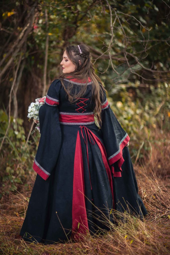 A woman in a red renaissance dress is standing in the woods.